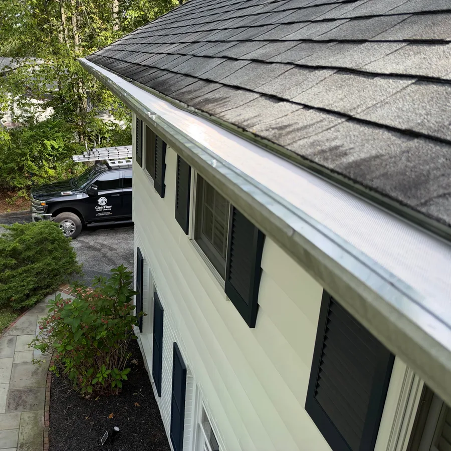 Gutter guard installed along the roofline of a two-story home with shutters and a ClearFlow truck parked below